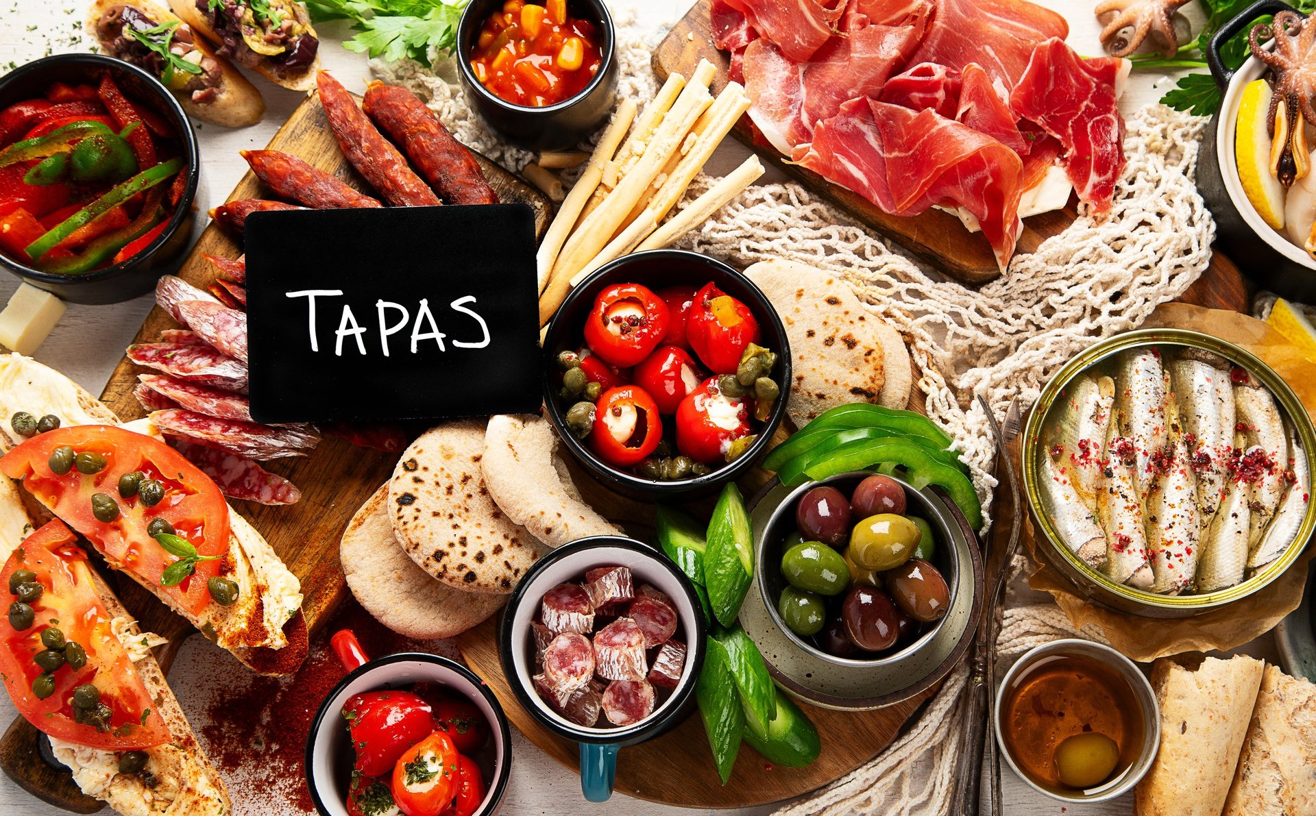 Spanish tapas sliced meat, ham, salami, olives and vegetables on a light background